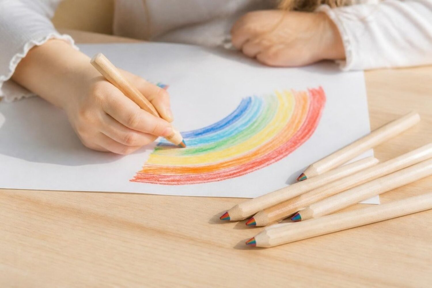 Kind malt mit Jumbo-Regenbogenstiften einen Regenbogen